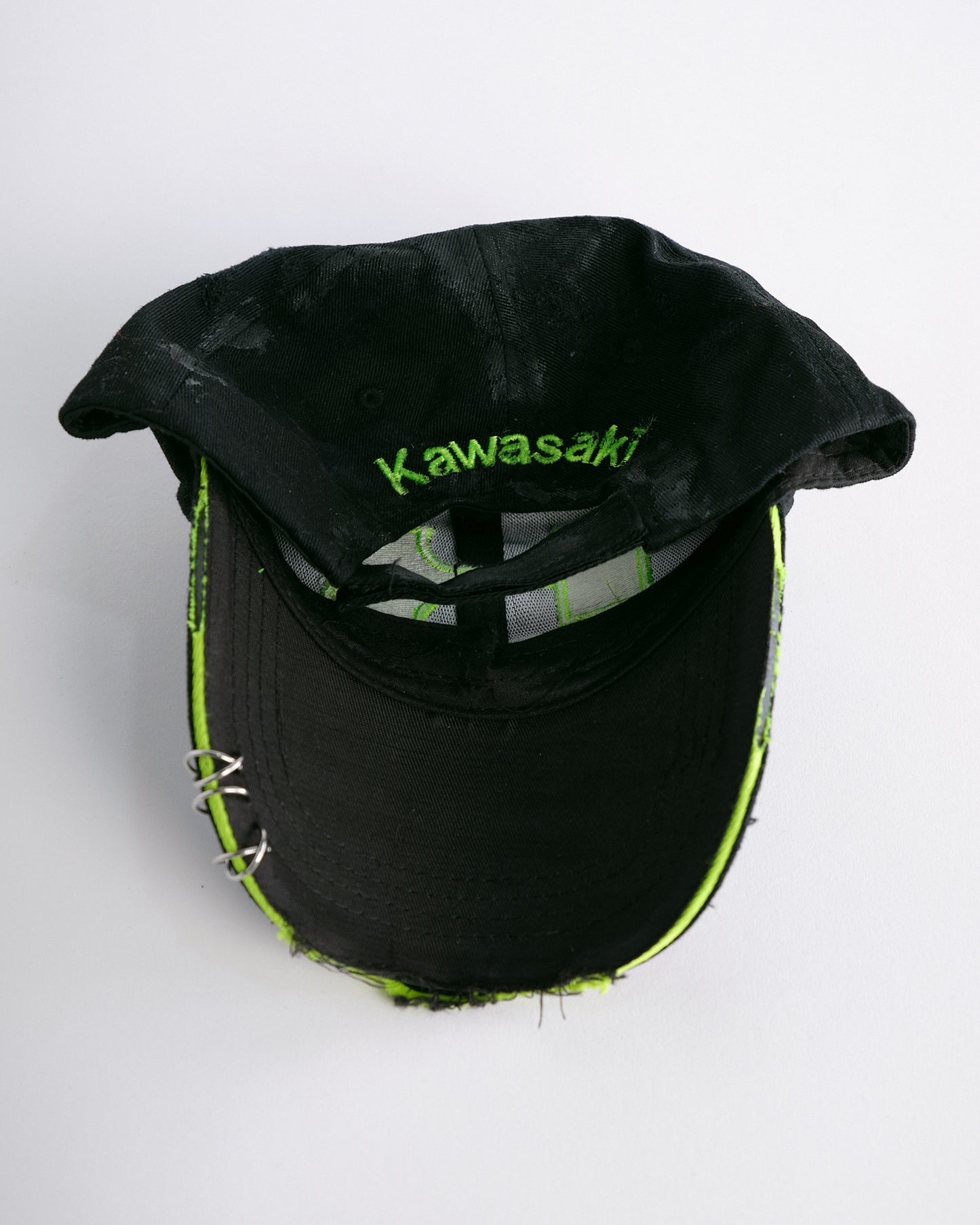 Back of ASTROBOI* x Kawasaki black hat with neon green rhinestone logo, resin finish, black paint distressing, and stainless steel piercings.