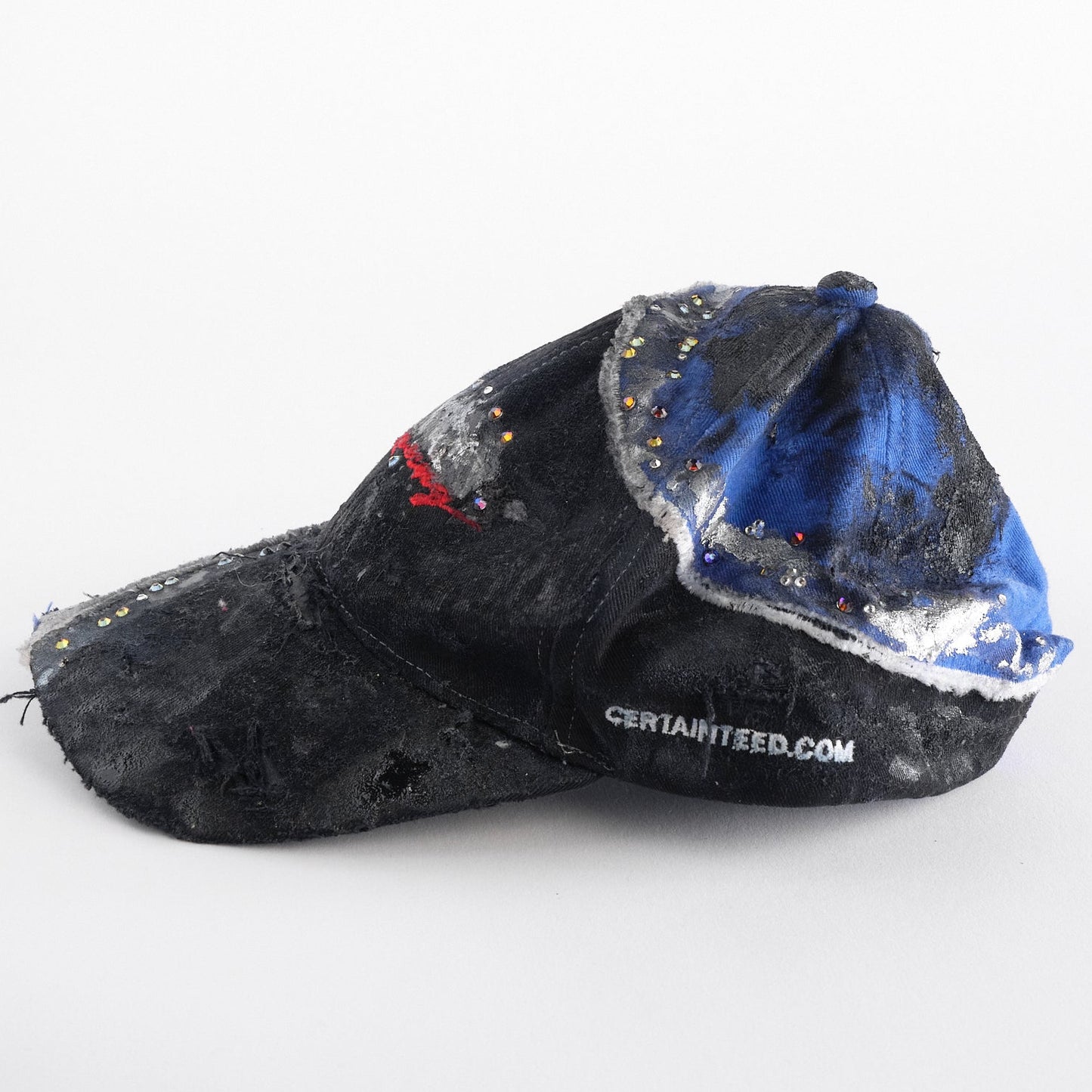 Left of ASTROBOI* black and blue distressed racing hat with metallic paint, rhinestones, and airbrushed details, handcrafted in NYC.