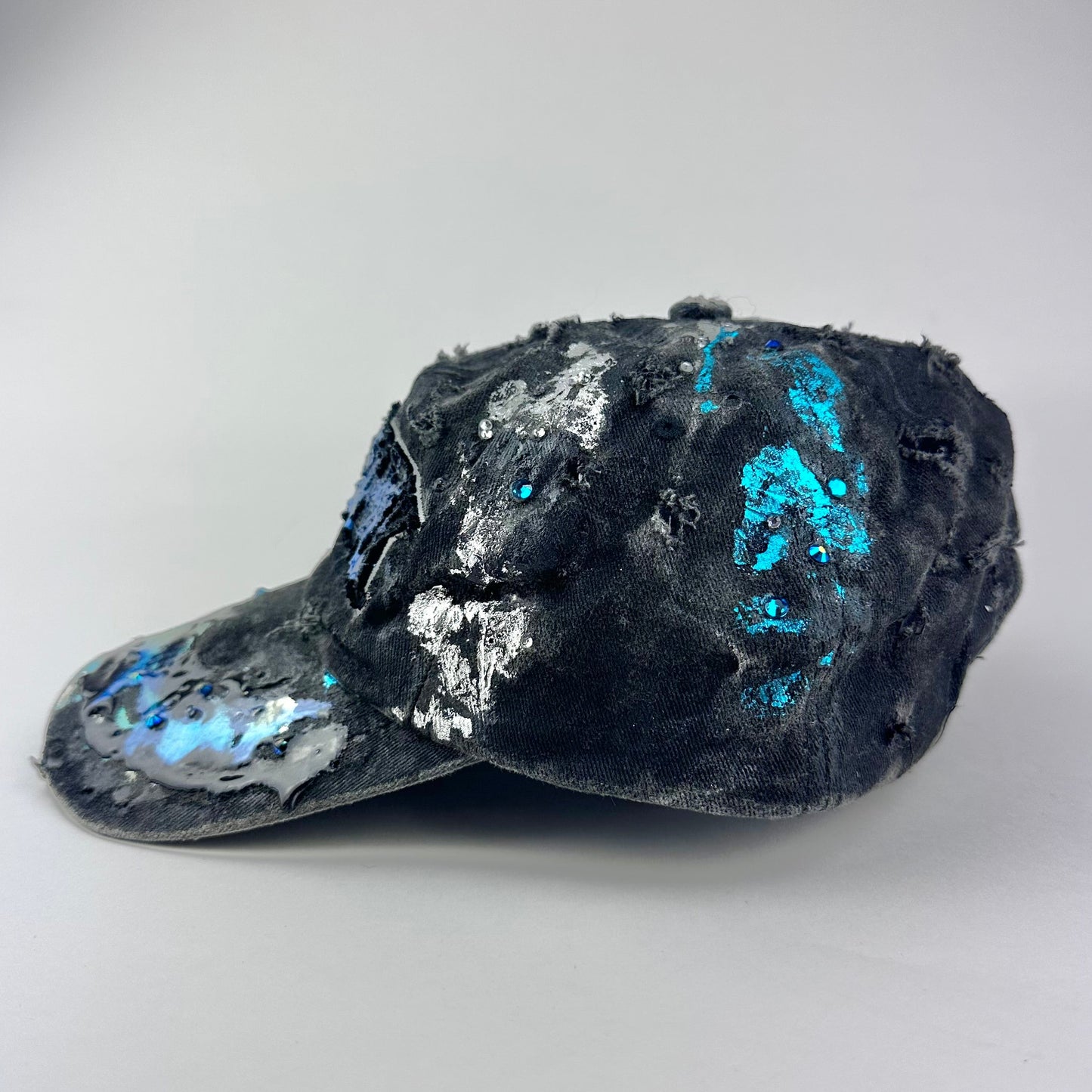 Left side of ASTROBOI* Plavala black iridescent hat with rhinestone NYC logos, metallic paint and black clear resin creating a hazy milky way effect.