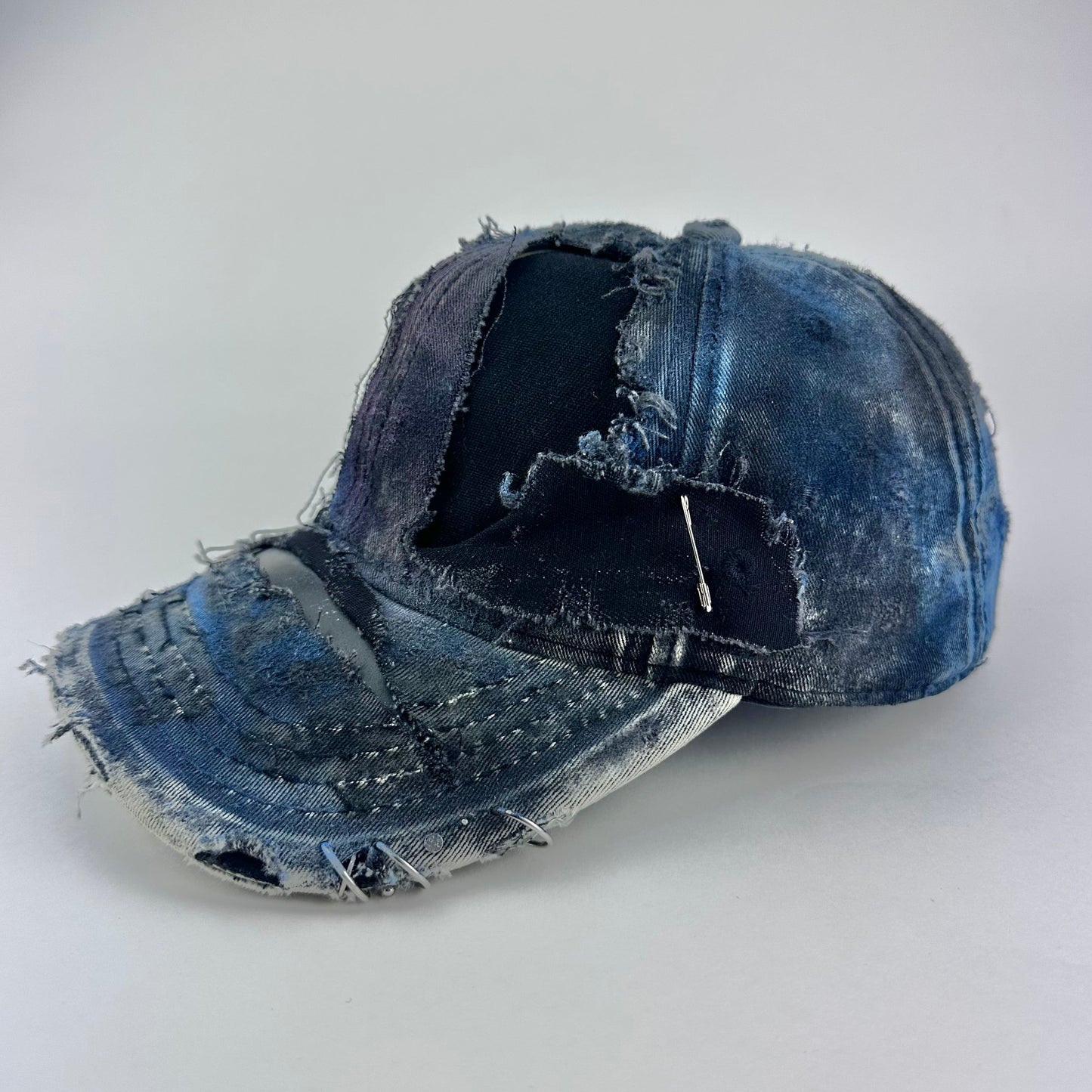 Left side of ASTROBOI* Nebulous Cloud black hat with rainbow airbrush denim, safety pins and silver steel piercings on distressed grunge design.