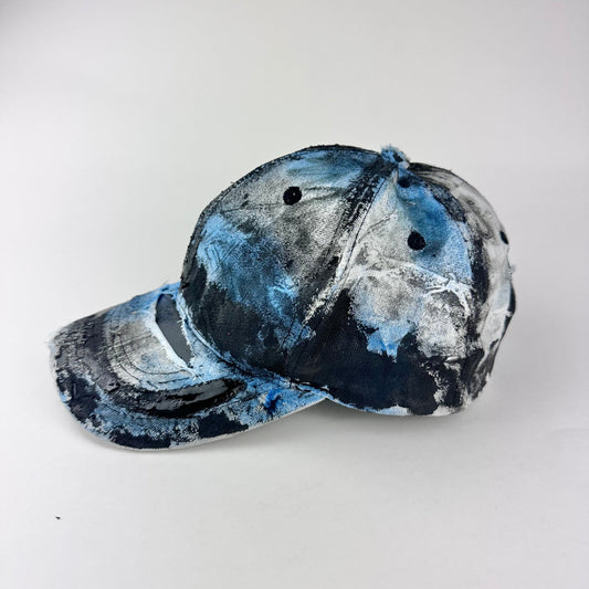 Left side of ASTROBOI* white trompe l’oeil denim print hat with blue and black paint, resin accents, and distressed detailing.