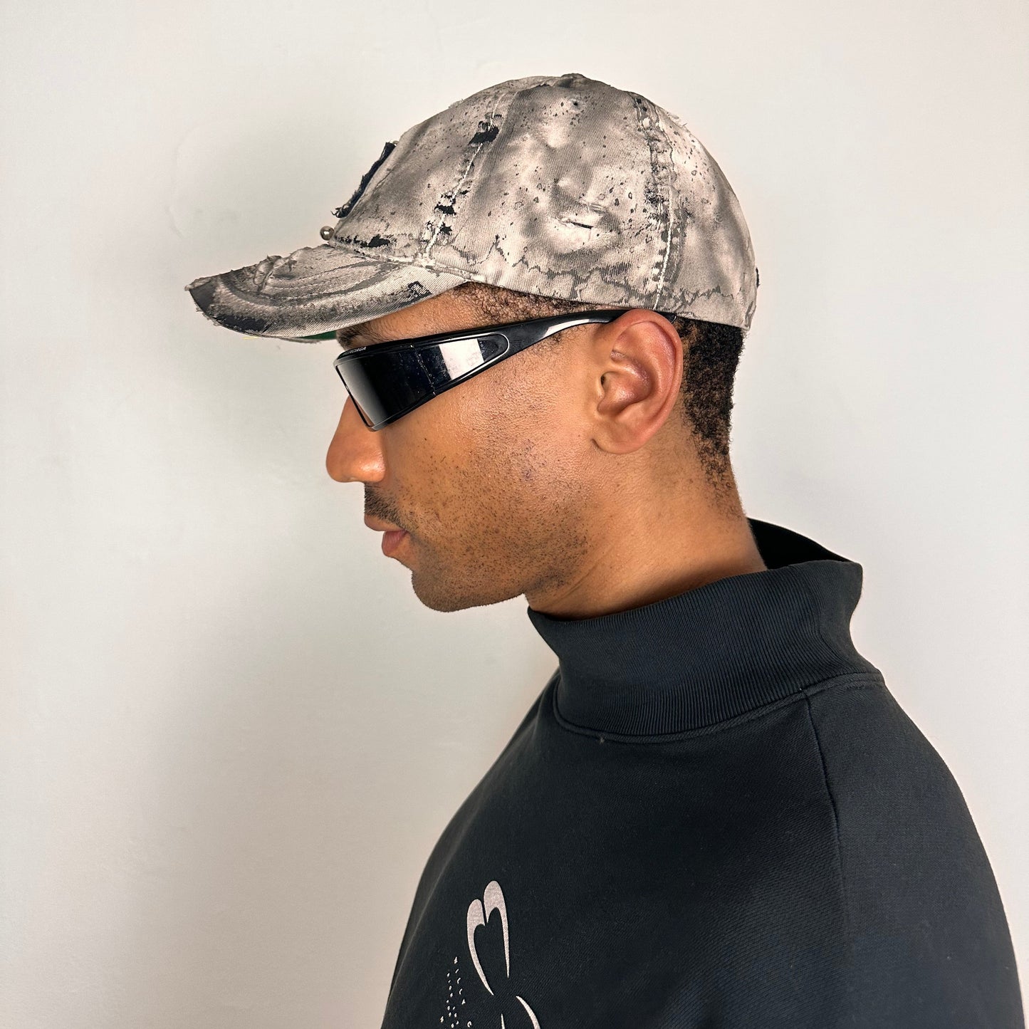 Left of Off-white and black faded ASTROBOI* x Abercrombie hat with custom paint treatment and stainless steel piercing, handmade in NYC.