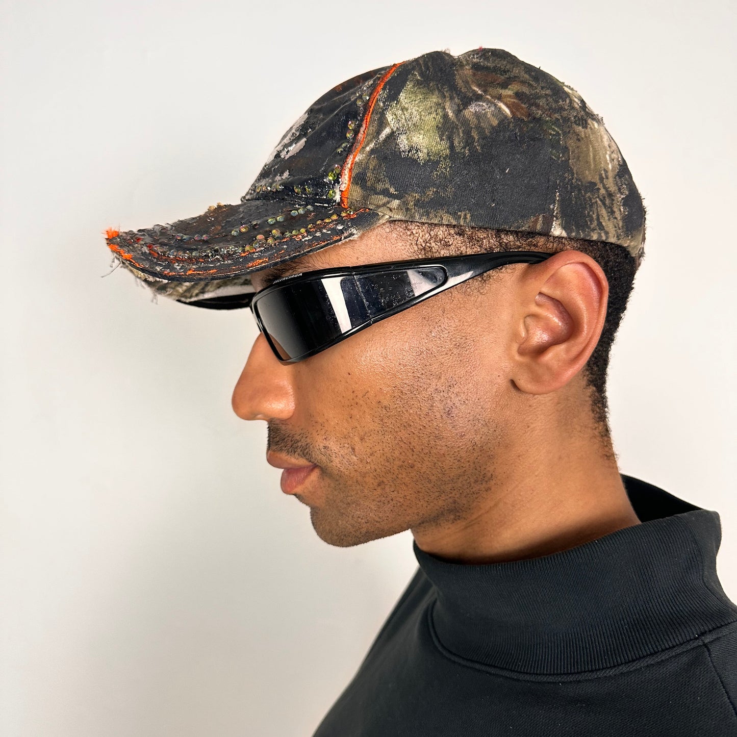 Left side of ASTROBOI* brown camouflage distressed hat with rhinestones sealed in clear resin and custom hand-painted detailing.