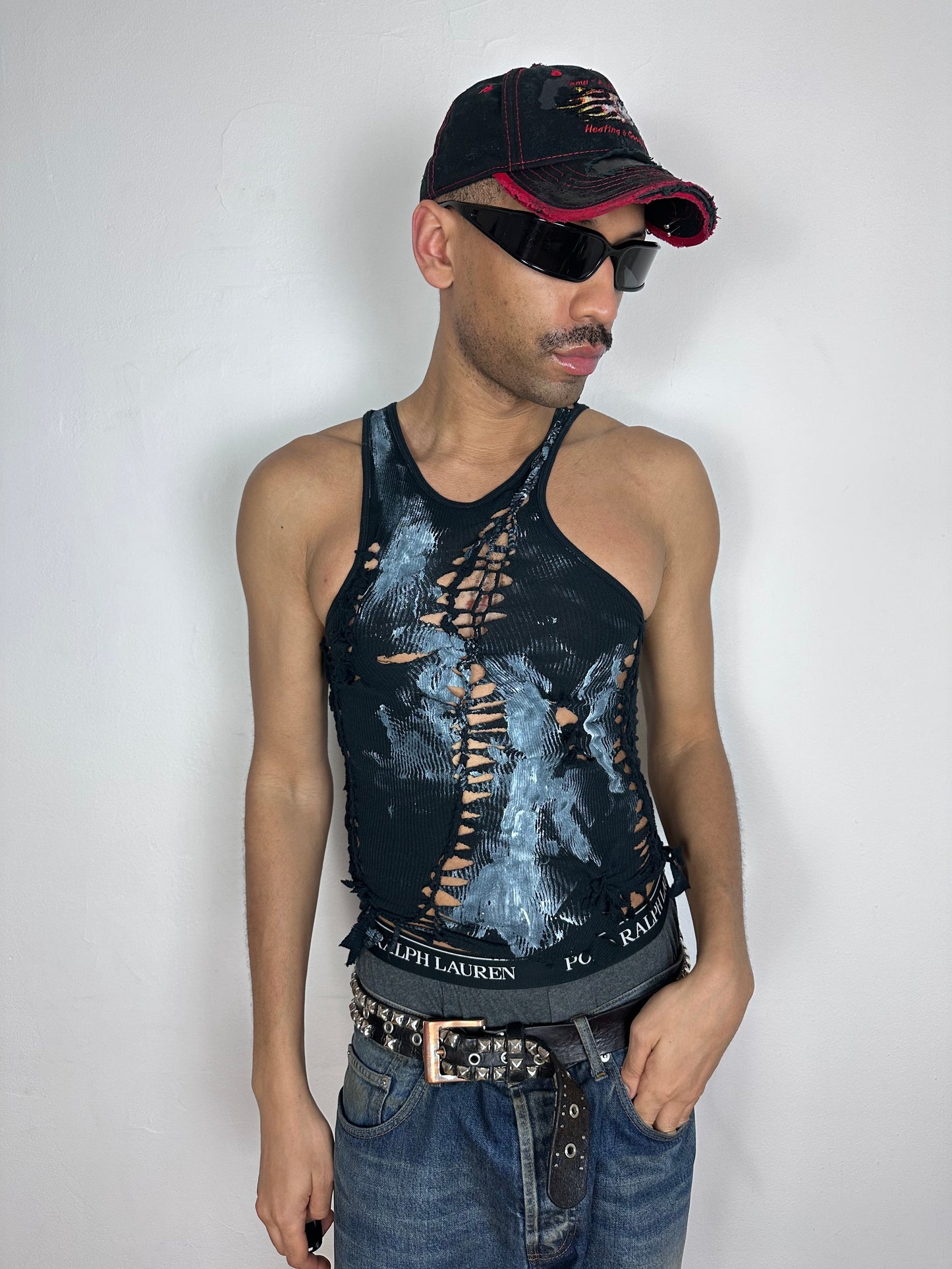 Male model wearing ASTROBOI* 'Shadow Play' black braided cut-out tank top with white paint splatter, styled full look, ASTROBOI* STUDIO NYC.
