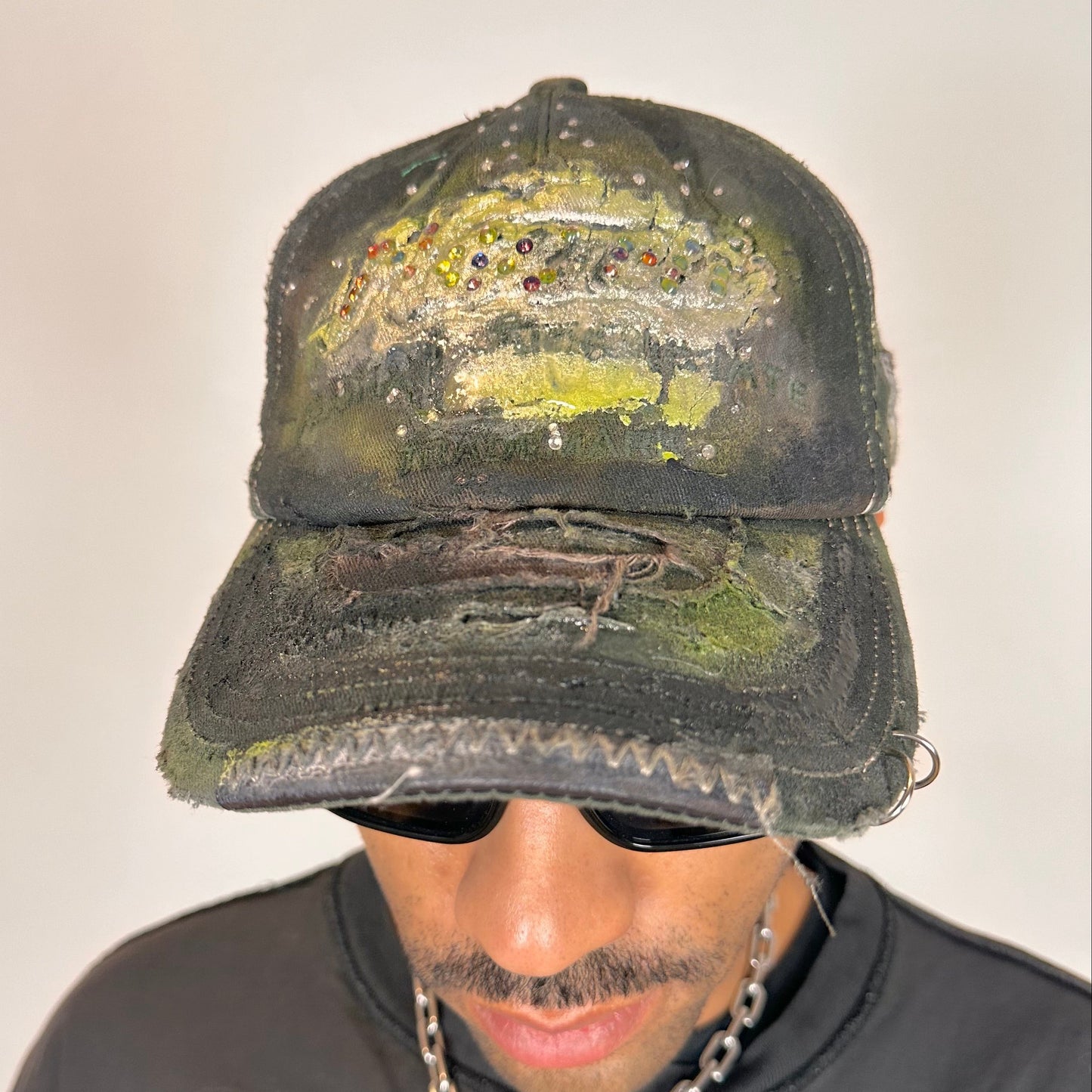 Front of “Green and brown distressed ASTROBOI* Hawaii hat with rhinestones, metallic paint, and sterling-steel piercings, customized in NYC.”