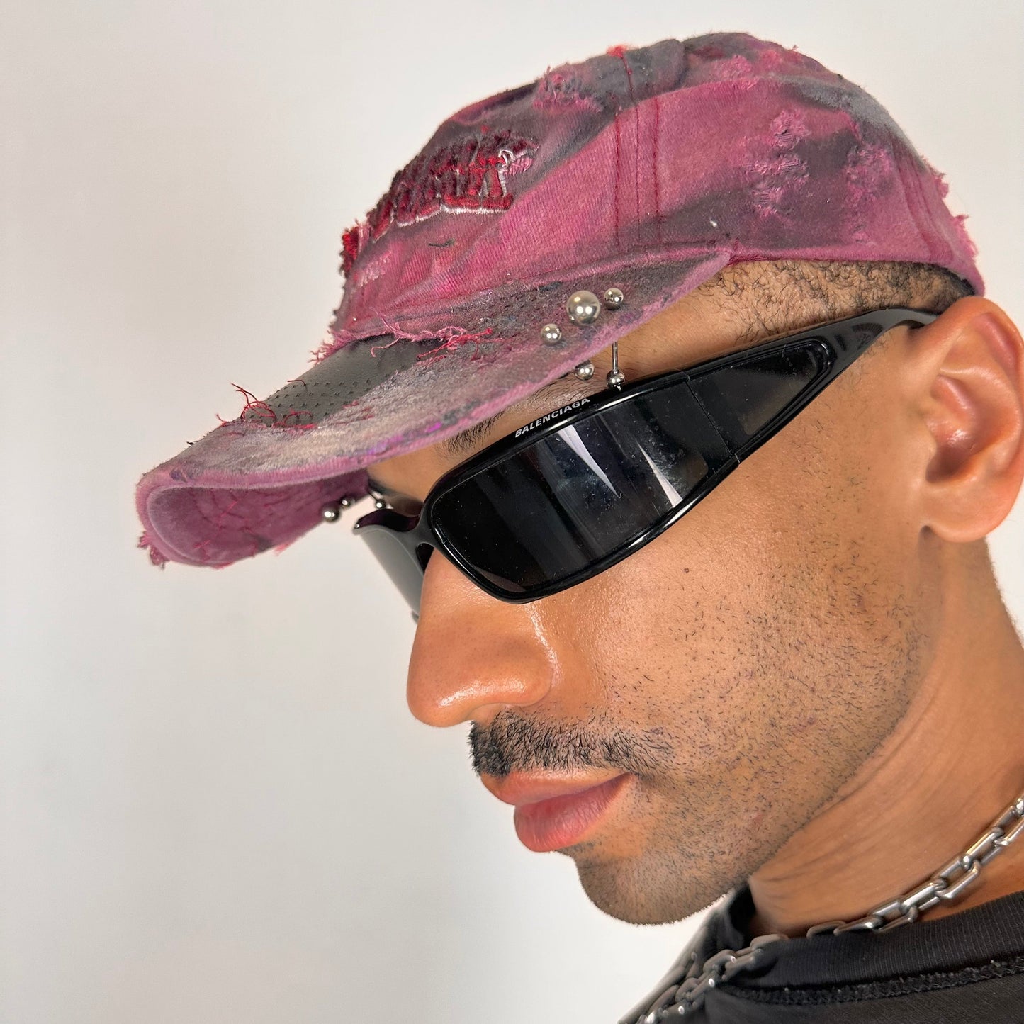 Piercing detail on ASTROBOI* Burn Out red New York hat with distressed finish, white and black paint details, and stainless steel piercings, adjustable back strap.