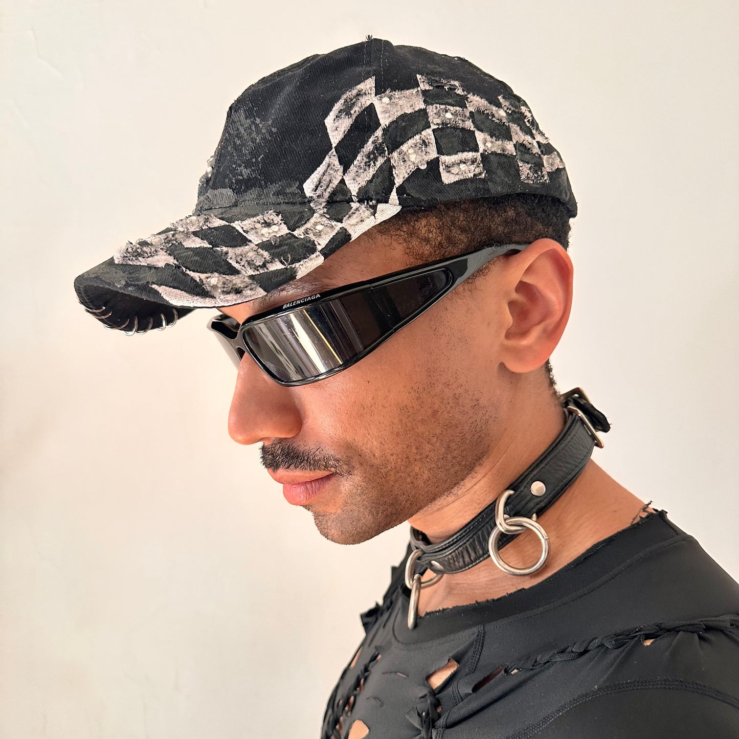 Front left detail on ASTROBOI* Speed Racing black and white checkered utility hat with resin-set rhinestones, stainless steel piercings, and hand-painted detailing