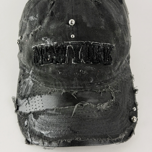 A distressed black baseball cap with a heavily ripped and frayed texture, featuring a sewn-on 'NEW YORK' patch on the front and silver metal studs.