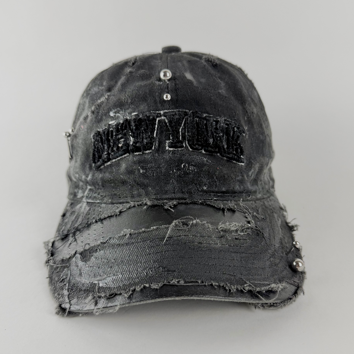ASTROBOI* 'New York Grunge' black distressed pierced hat with 'New York' embroidered logo at front, black paint details, and stainless steel piercings, front view.