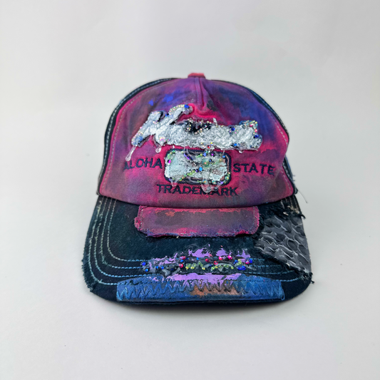 ASTROBOI* 'Tropicale' red and black Y2K Hawaii rhinestone hat with silver embroidered 'Hawaii ALOHA STATE TRADEMARK' text, purple and pink paint splatter, and metallic rhinestone embellishments, front view two.