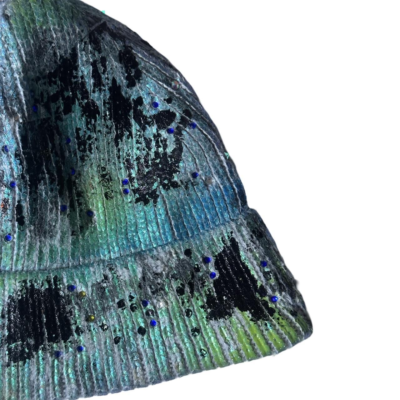 Right side of ASTROBOI* blue-green iridescent beanie featuring black metallic paint accents and tonal rhinestones, custom-made in NYC for a bold streetwear look.
