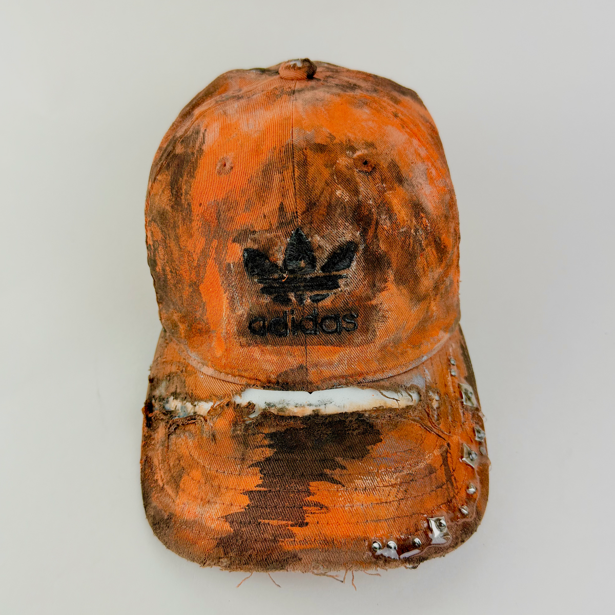 ASTROBOI* x Adidas 'Black Sun' orange and black painted studded rhinestone hat with black painted Adidas logo at center front, faded abstract design, and rhinestone embellishments, front view.