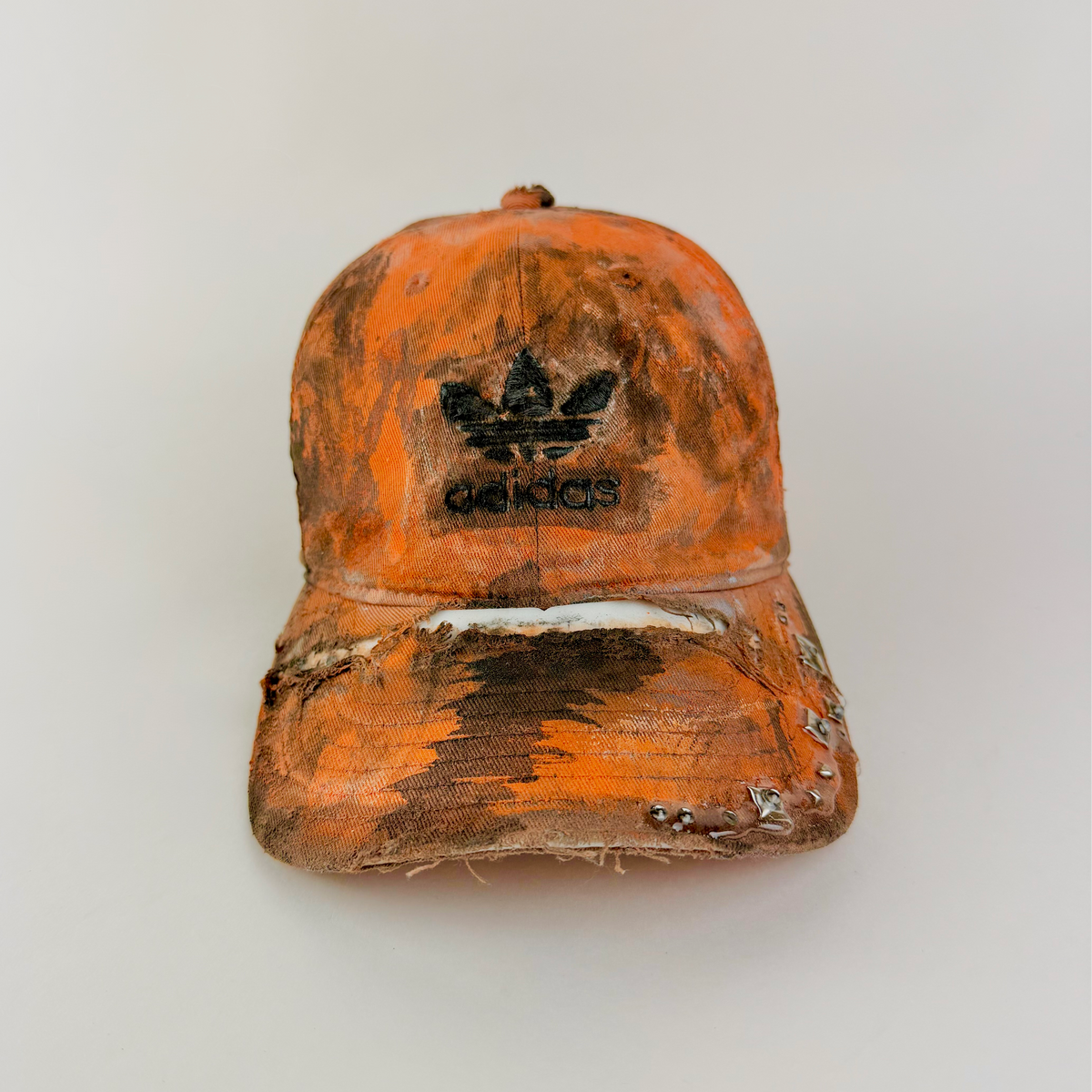 ASTROBOI* x Adidas 'Black Sun' orange and black painted studded rhinestone hat with black painted Adidas logo at center front, faded abstract design, and rhinestone embellishments, front view.