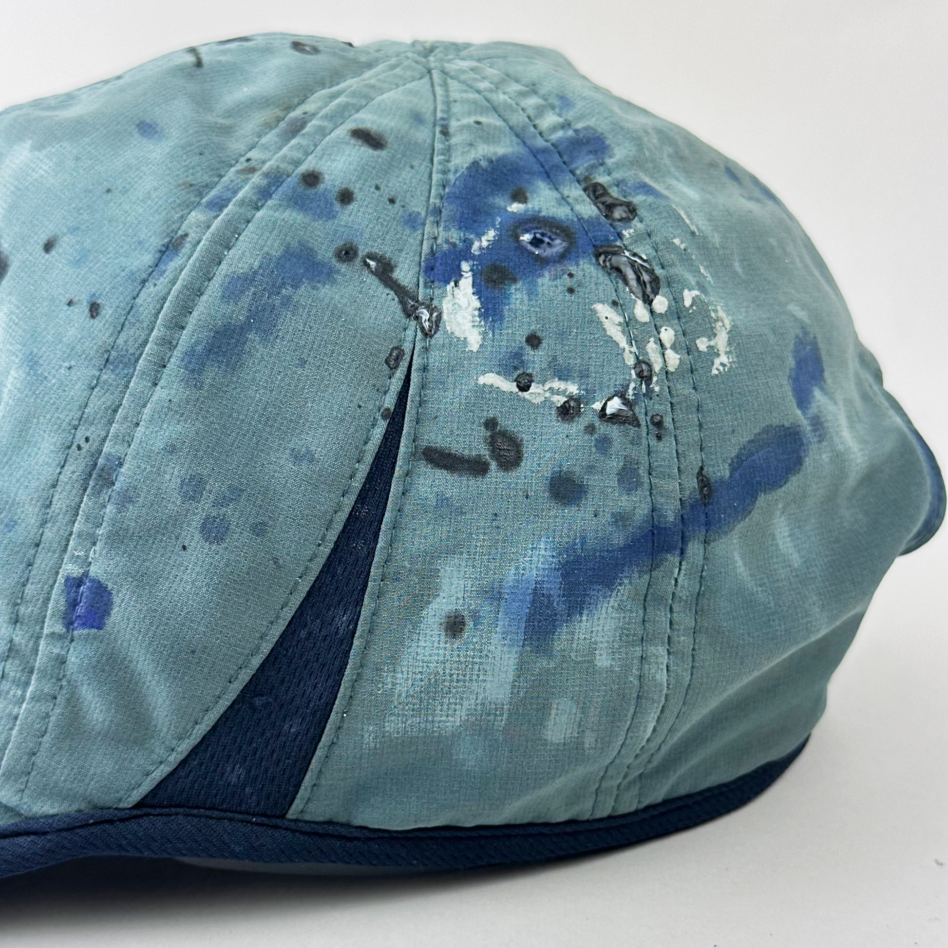 Back detail of ASTROBOI* x Adidas 'Haaland' showing raised faded paint treatment and blue visor trim detail on blue and black cap.