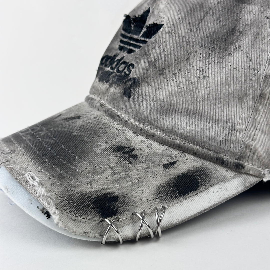 ASTROBOI* x Adidas 'H Chic' showing Adidas logo, black paint detailing, distressed finish, and stainless steel piercing detail close up on tan base.