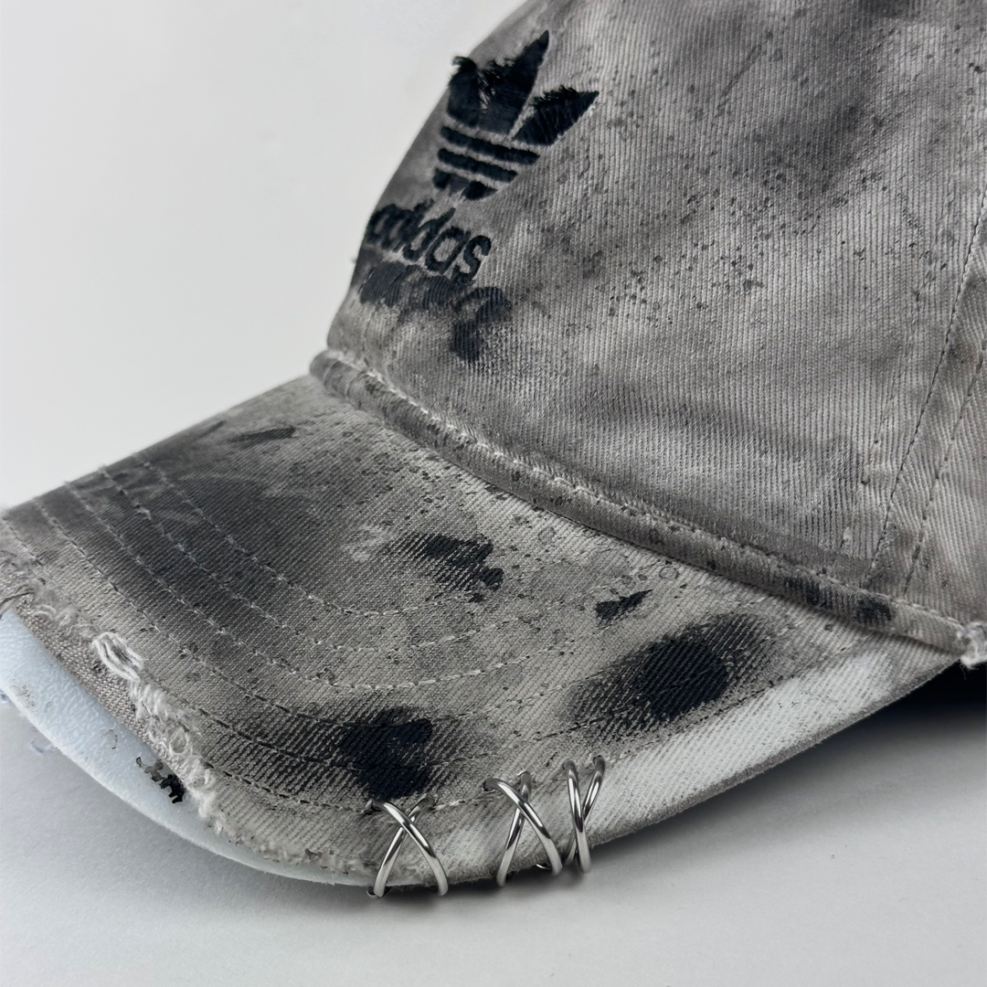 ASTROBOI* x Adidas 'H Chic' showing Adidas logo, black paint detailing, distressed finish, and stainless steel piercing detail close up on tan base.