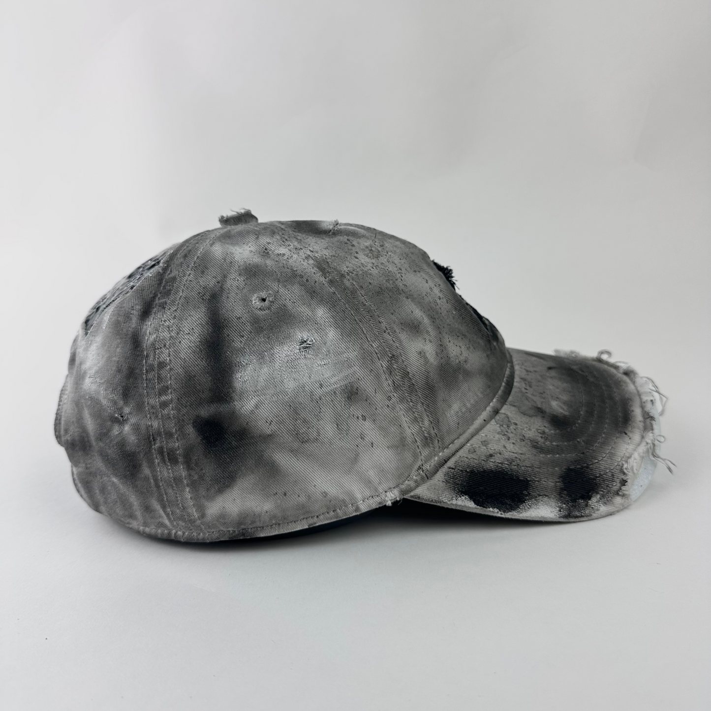 Left side detail of ASTROBOI* x Adidas 'H Chic' showing black paint detailing, distressing, and piercing construction on tan hat.