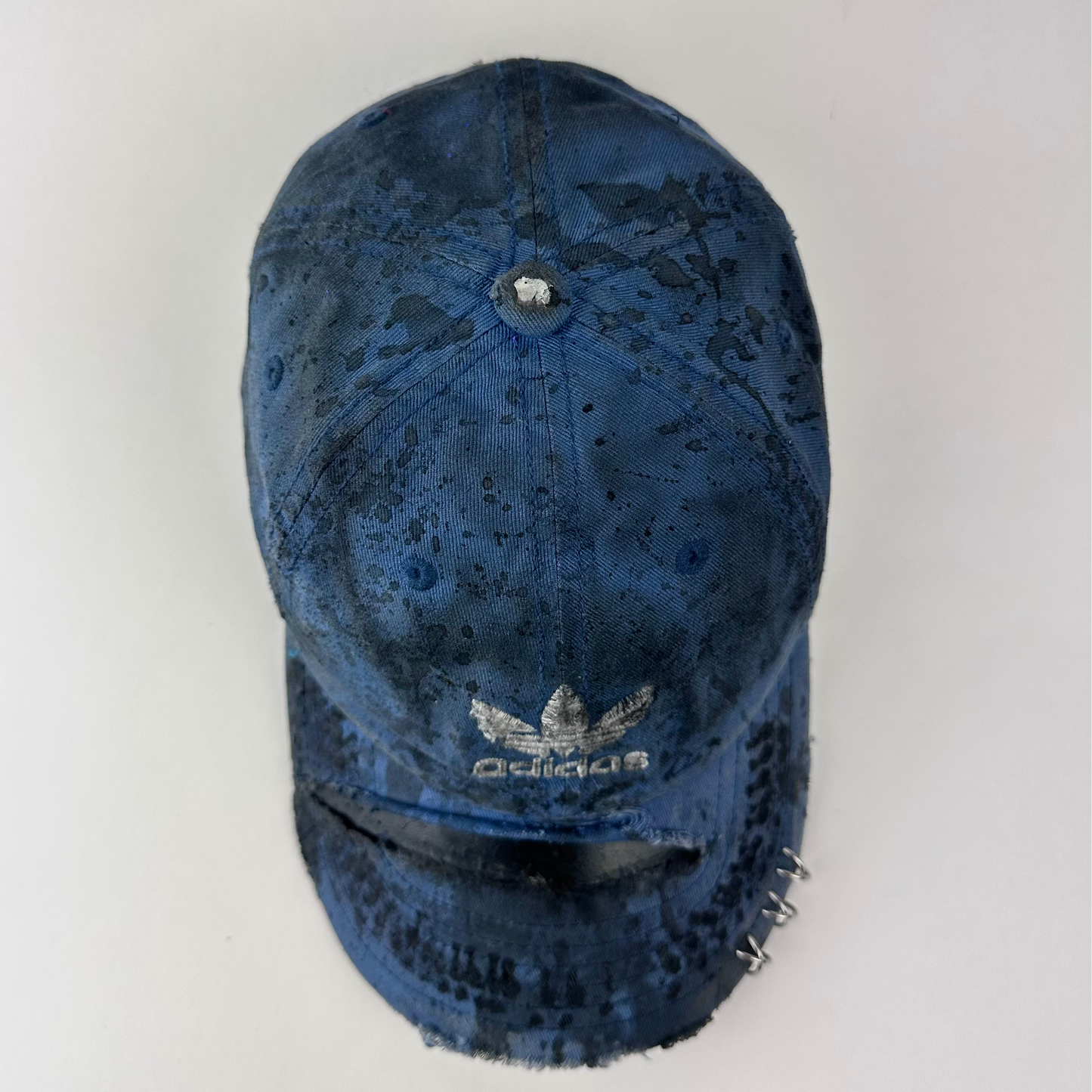 ASTROBOI* x Adidas 'H Chic' tan distressed grunge hat with black paint detailing, distressing, and Adidas logo at front, stainless steel piercings, topview.
