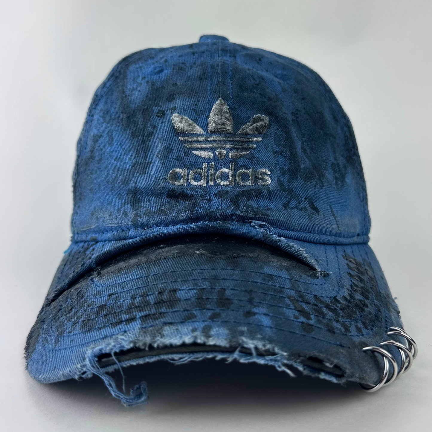 ASTROBOI* x Adidas 'H Chic' tan distressed grunge hat with black paint detailing, distressing, and Adidas logo at front, stainless steel piercings, front view.