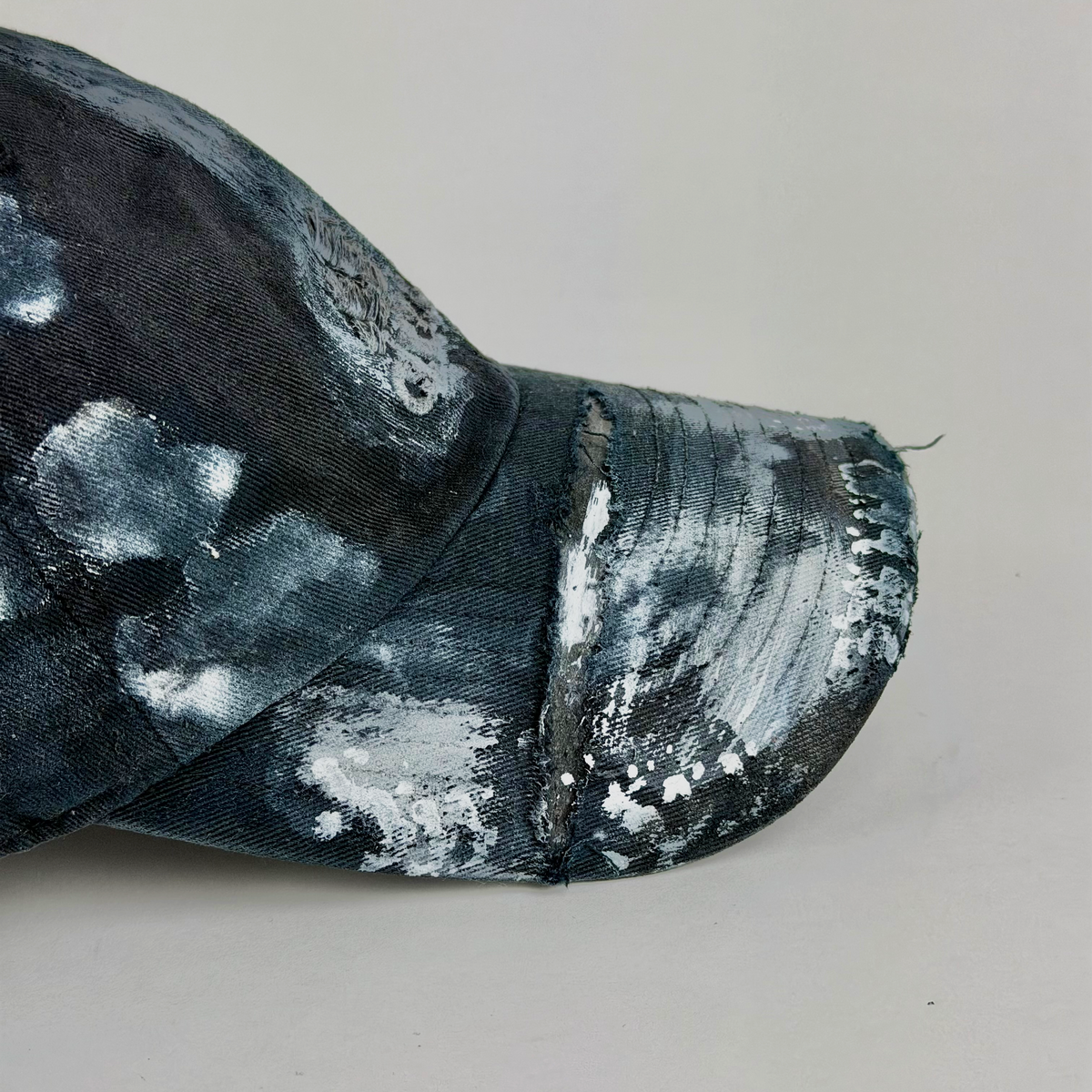 A close-up of a baseball cap with a distressed, painted finish in black and white, showing the side and brim against a plain light gray background.