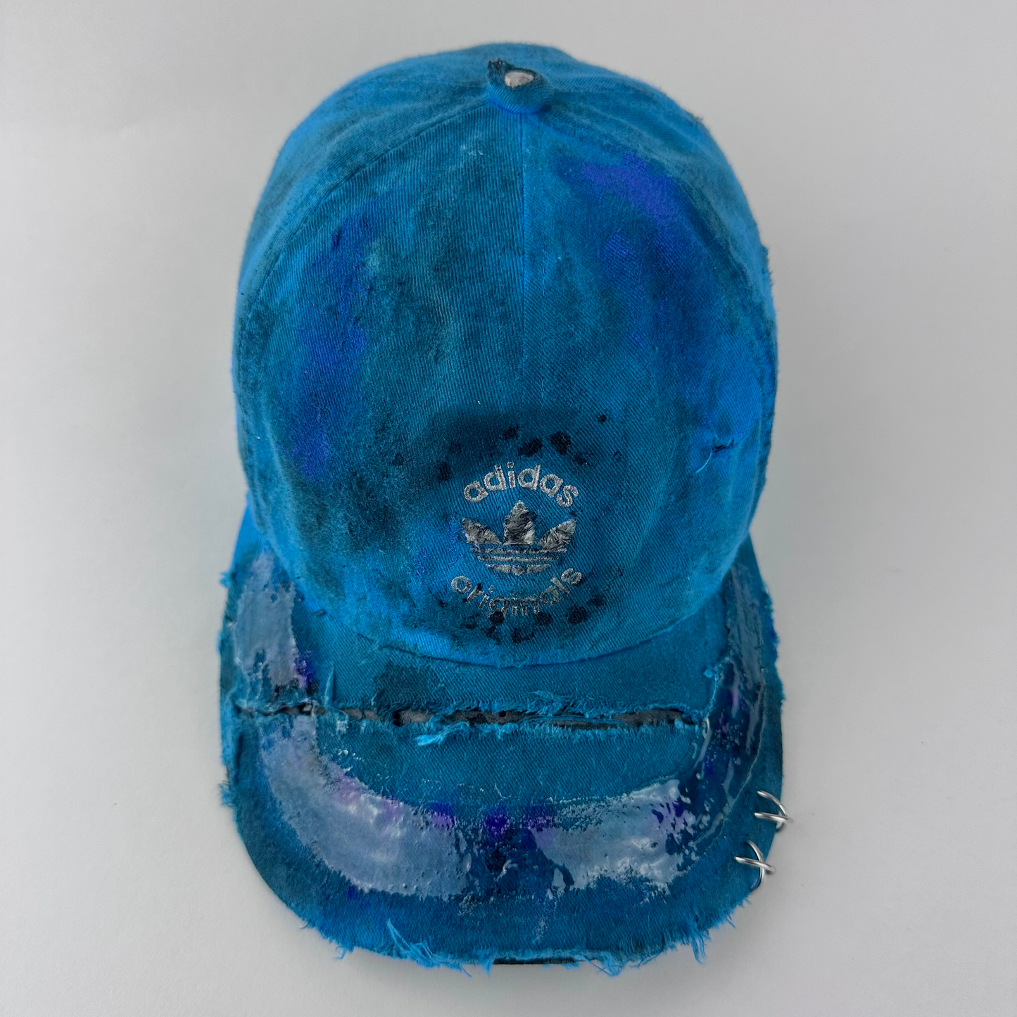 ASTROBOI* x Adidas 'Nebula' blue distressed pierced hat with white Adidas logo at front, custom paint treatment, stainless steel piercings, and resin 3D visor finish, front view.