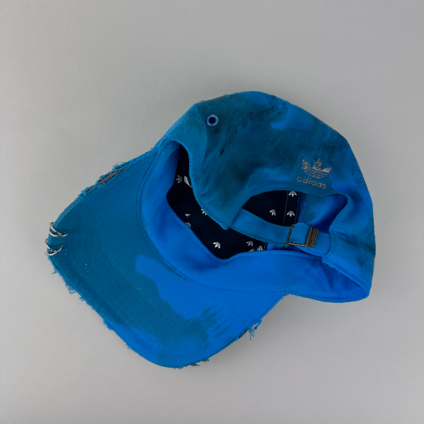 ASTROBOI* x Adidas 'Nebula' blue distressed pierced hat, rear view showing white Adidas back logo and adjustable strap.