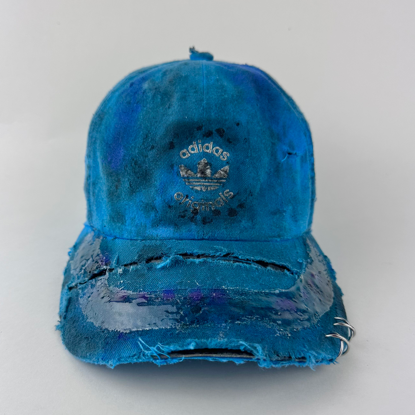 ASTROBOI* x Adidas 'Nebula' blue distressed pierced hat with white Adidas logo at front, custom paint treatment, stainless steel piercings, and resin 3D visor finish, front view.