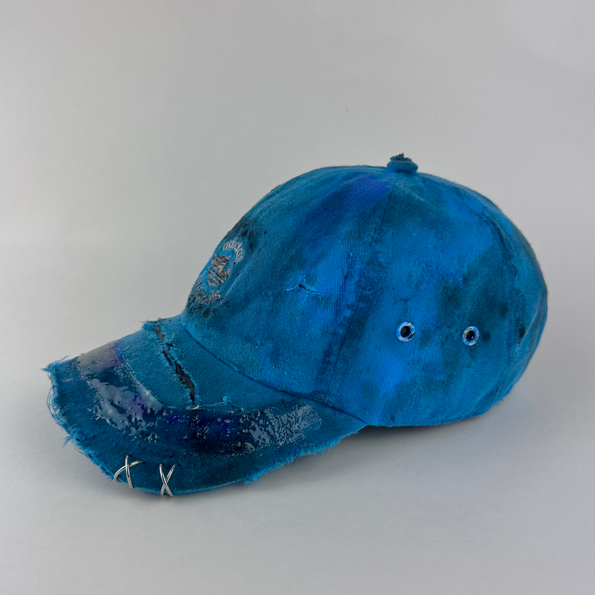 Left side detail of ASTROBOI* x Adidas 'Nebula' showing distressing, custom paint treatment, and resin visor detail on blue Adidas hat.