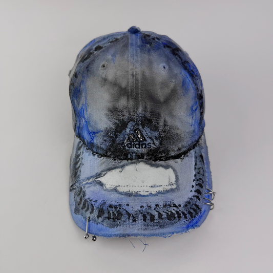 ASTROBOI* x Adidas 'Psykos' white blue and black tie-dye painted grunge cap with rhinestone-embellished Adidas logo, black and blue faded abstract design, stainless steel piercings, and deconstructed visor, front view.