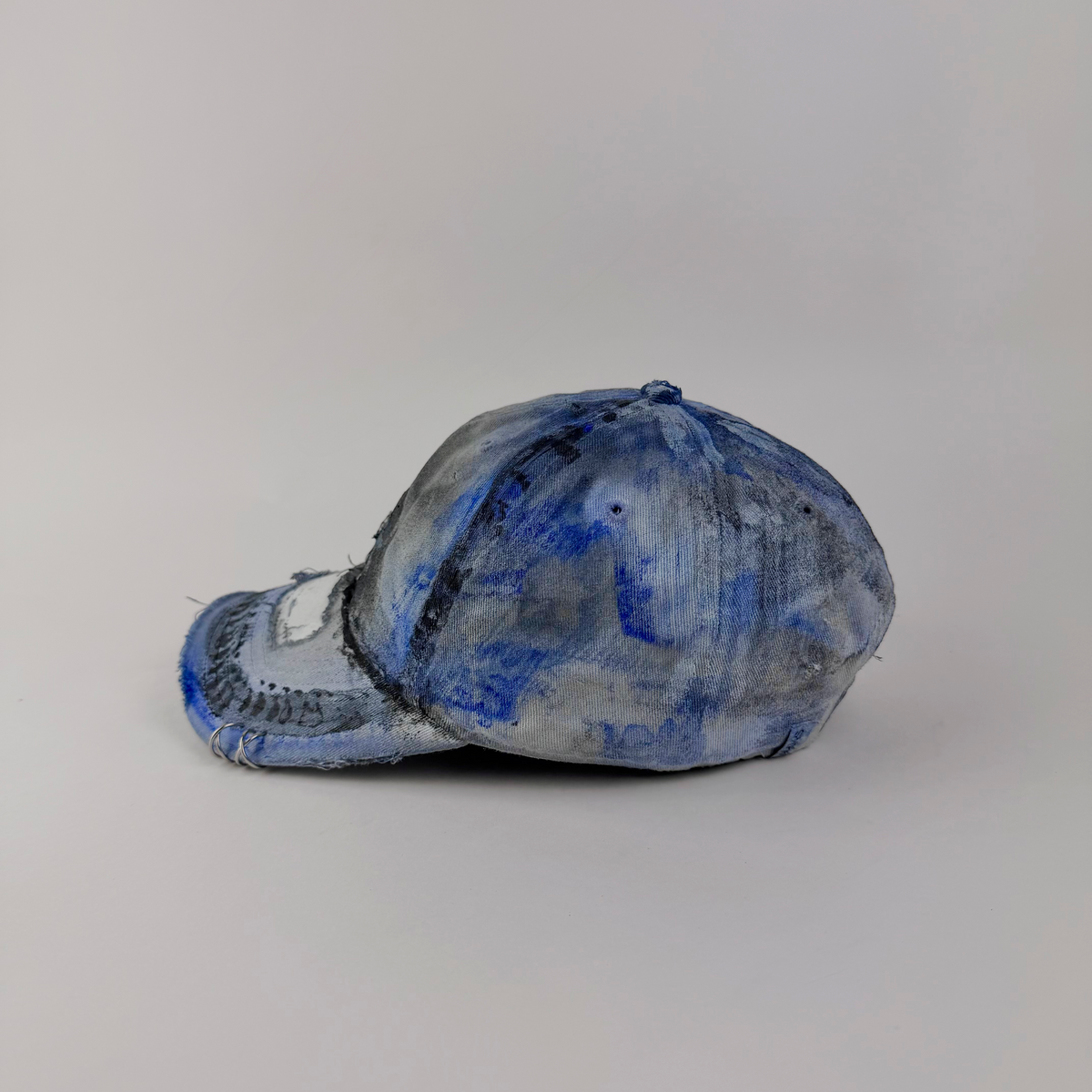 Left side detail of ASTROBOI* x Adidas 'Psykos' showing black and blue tie-dye faded design, piercing detail, and deconstructed visor on grunge cap.