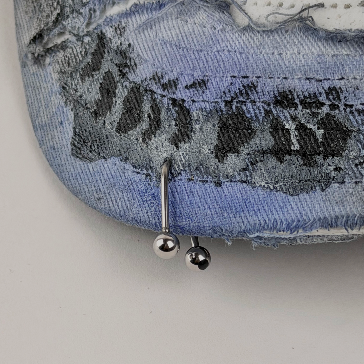 Two silver ball stud earrings shown on a distressed blue denim surface with visible frayed and faded fabric texture.