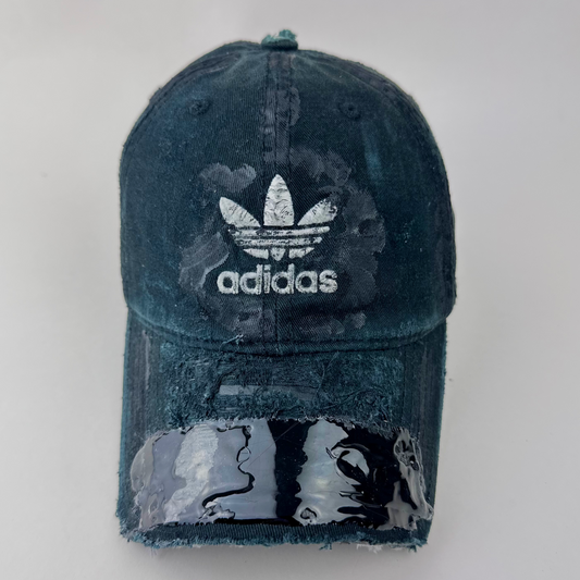 ASTROBOI* x Adidas 'Washed' black distressed faded cap with navy blue fade, custom paint treatment, partially sawed-off visor, and Adidas trefoil logo at center front, front view.