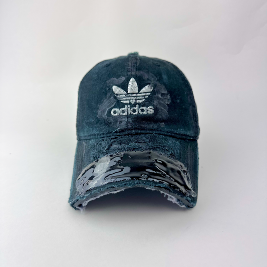 ASTROBOI* x Adidas 'Washed' black distressed faded cap with navy blue fade, custom paint treatment, partially sawed-off visor, and Adidas trefoil logo at center front, front view two.