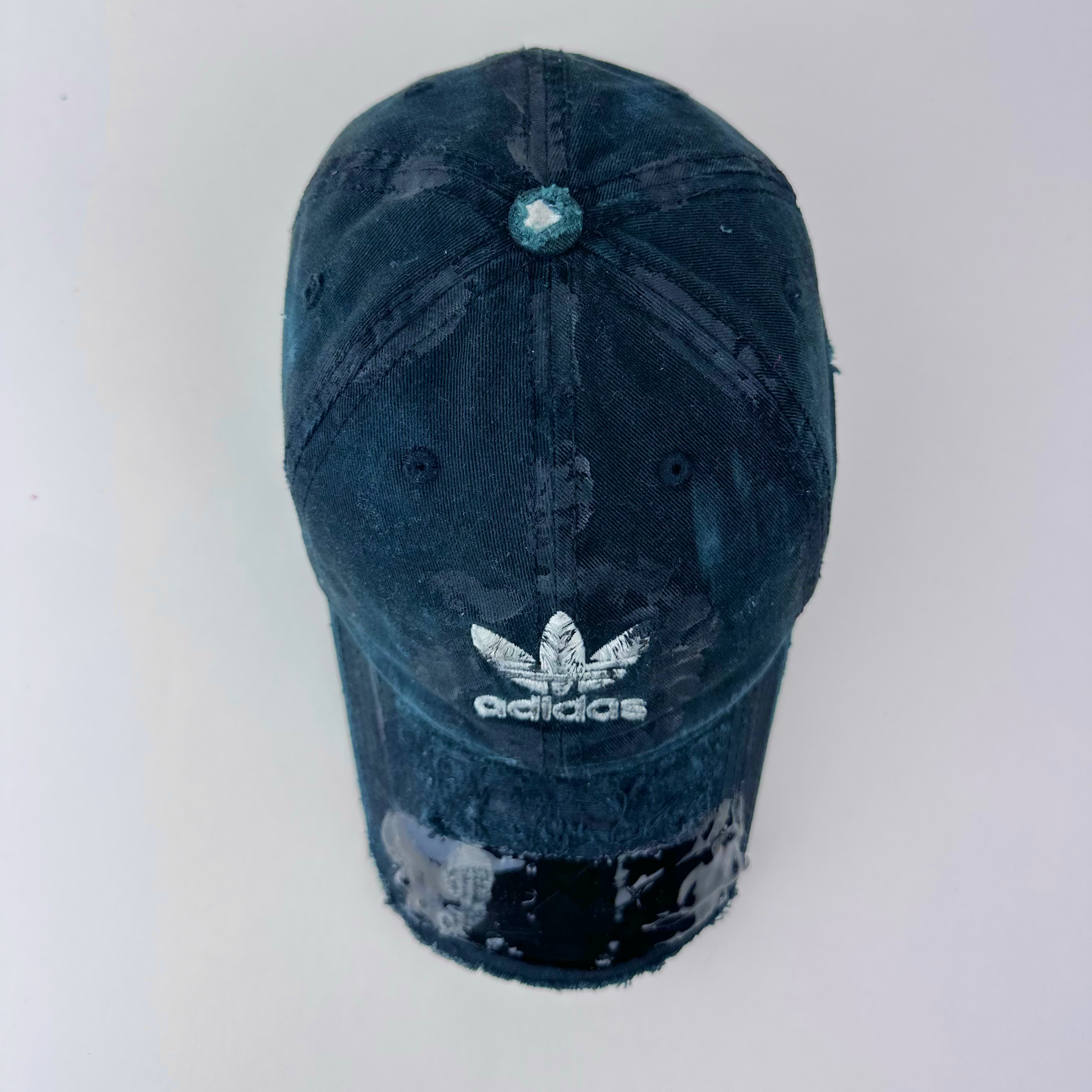 Top view of ASTROBOI* x Adidas 'Washed' showing Adidas trefoil logo, black to navy fade, and melted duct tape sealed under resin on partially sawed-off visor.