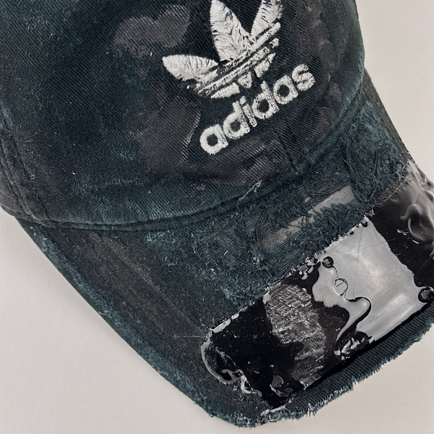 Close-up of visor detail on ASTROBOI* x Adidas 'Washed' showing Adidas trefoil logo, black to navy fade, and melted duct tape sealed under resin on partially sawed-off visor.