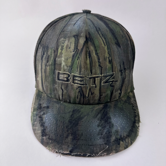 ASTROBOI* x Betz brown Real Tree camouflage doodle hat with hand drawn design, custom paint treatment, and Betz logo at front, front view.