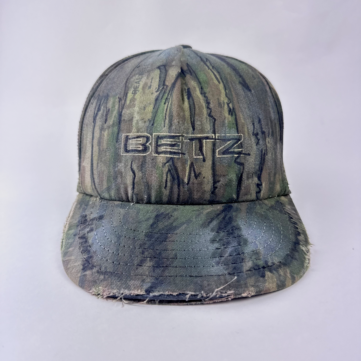 ASTROBOI* x Betz brown Real Tree camouflage doodle hat with hand drawn design, custom paint treatment, and Betz logo at front, front view.