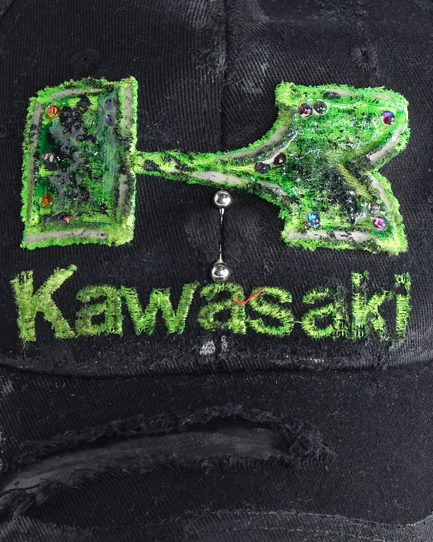 Logo on ASTROBOI* x Kawasaki black hat with neon green rhinestone logo, resin finish, black paint distressing, and stainless steel piercings.