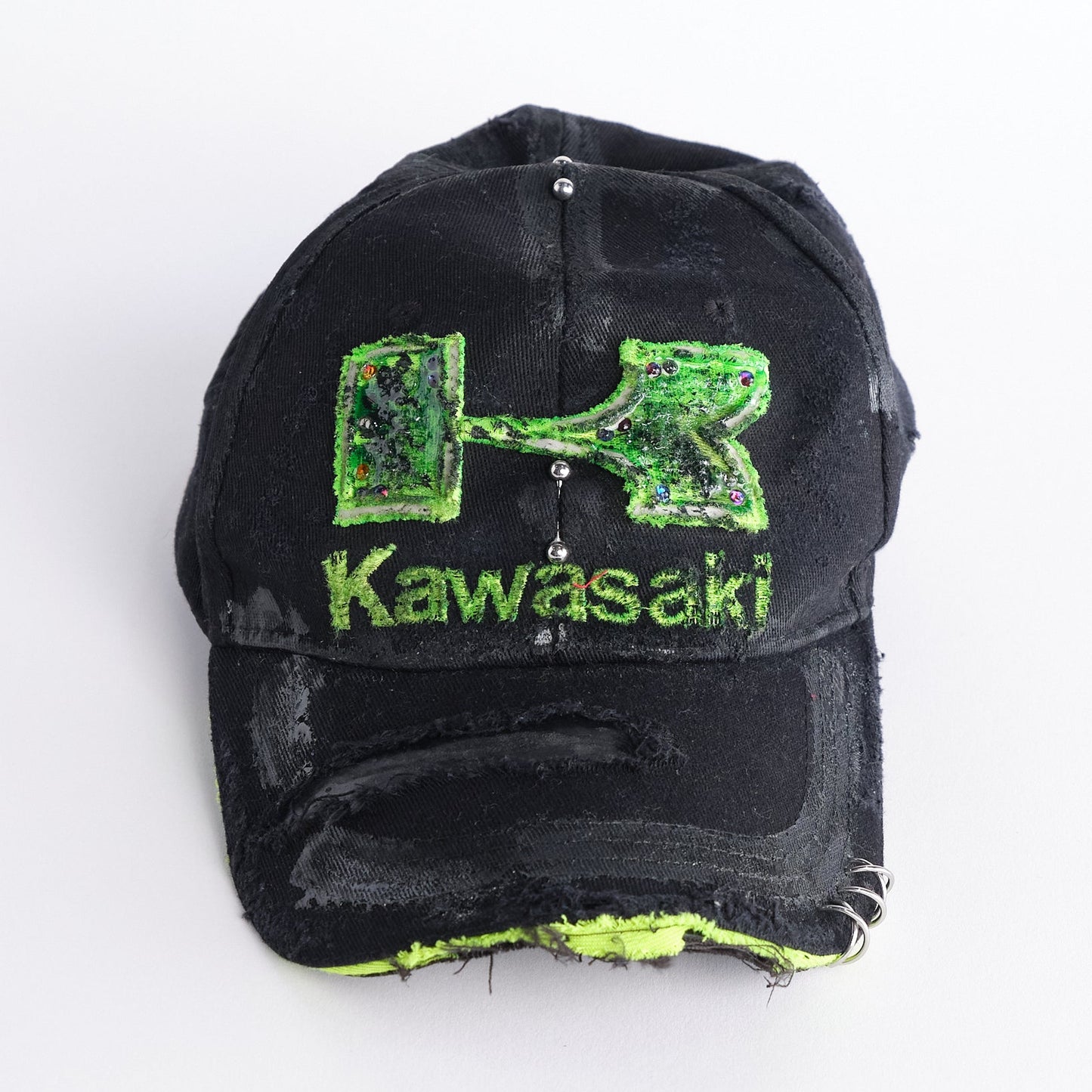 Front of ASTROBOI* x Kawasaki black hat with neon green rhinestone logo, resin finish, black paint distressing, and stainless steel piercings.