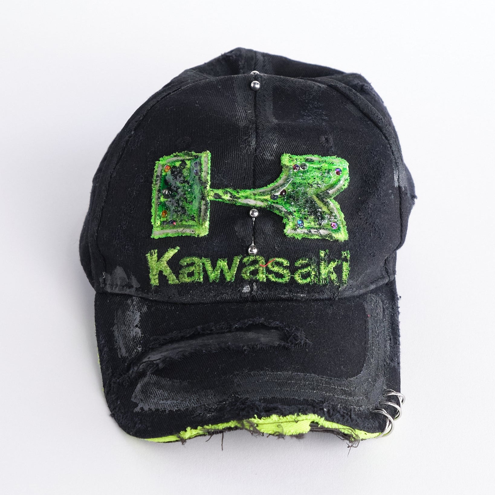 Front of ASTROBOI* x Kawasaki black hat with neon green rhinestone logo, resin finish, black paint distressing, and stainless steel piercings.