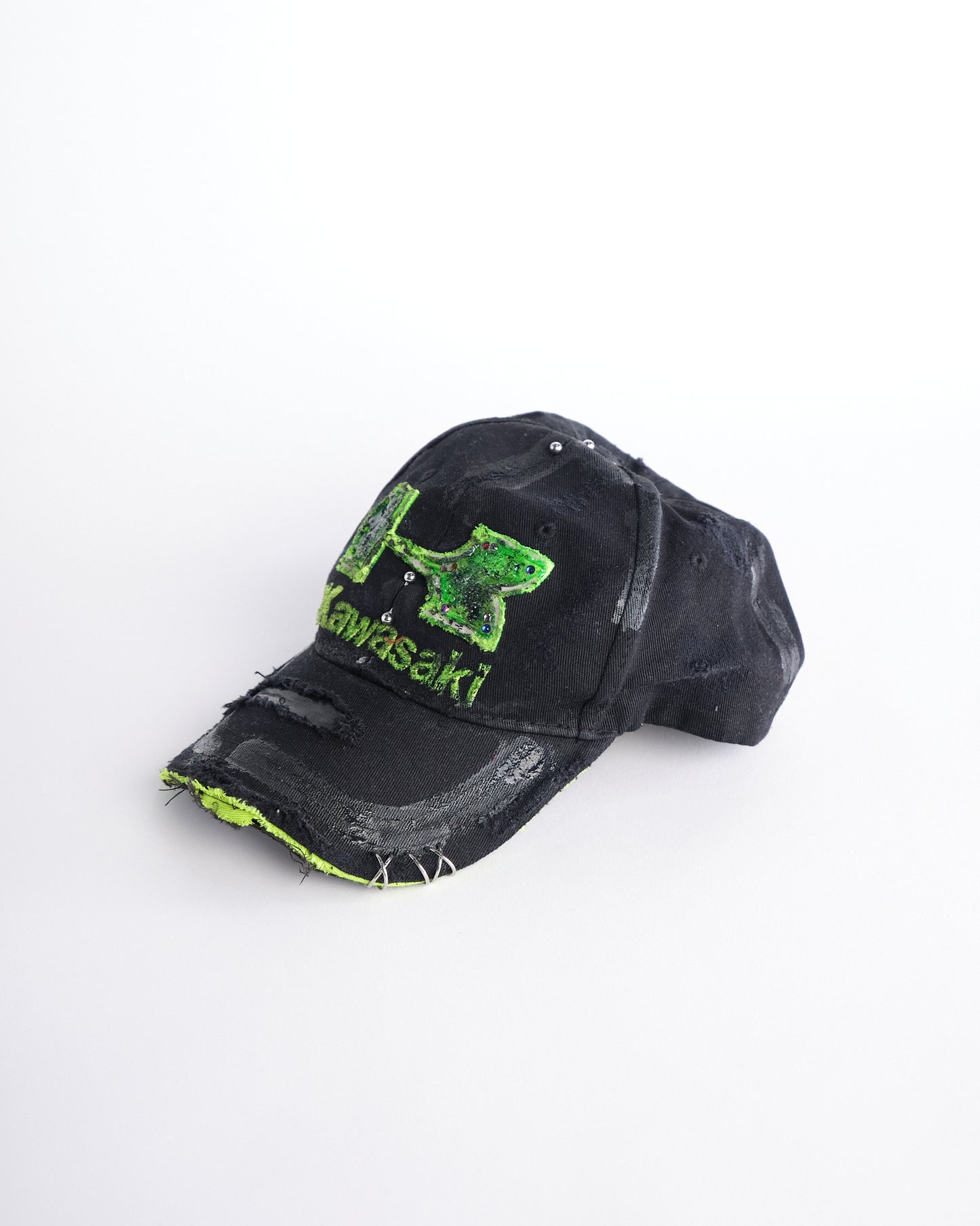 Front left of ASTROBOI* x Kawasaki black hat with neon green rhinestone logo, resin finish, black paint distressing, and stainless steel piercings.