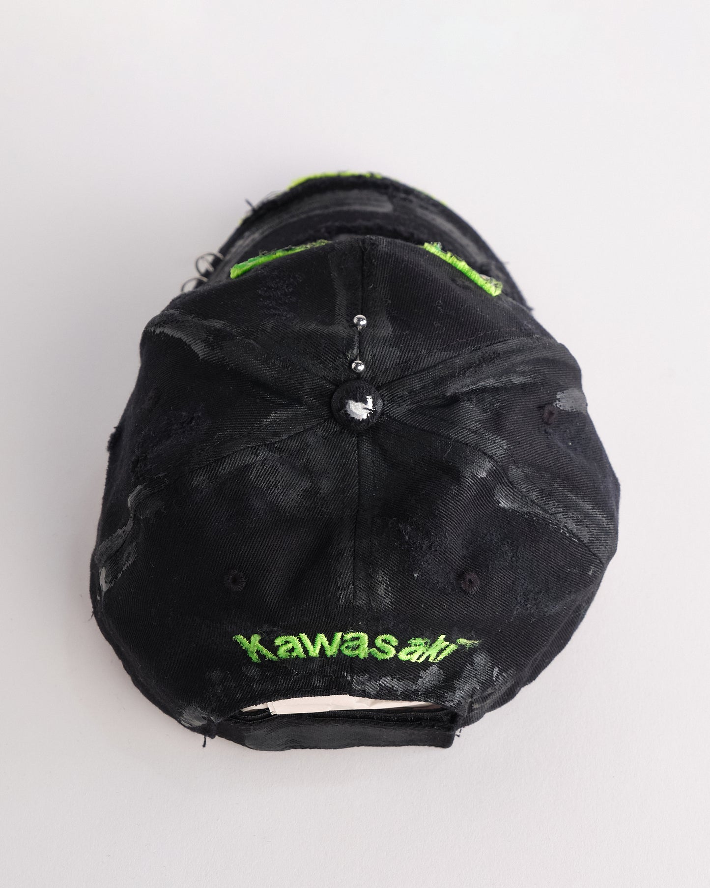 Top of ASTROBOI* x Kawasaki black hat with neon green rhinestone logo, resin finish, black paint distressing, and stainless steel piercings.