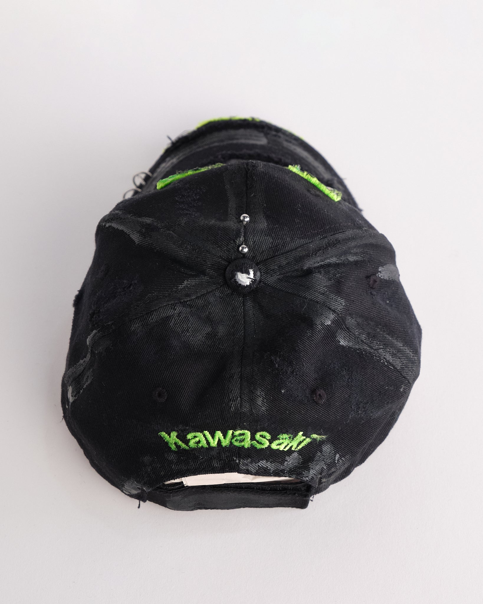 Top of ASTROBOI* x Kawasaki black hat with neon green rhinestone logo, resin finish, black paint distressing, and stainless steel piercings.