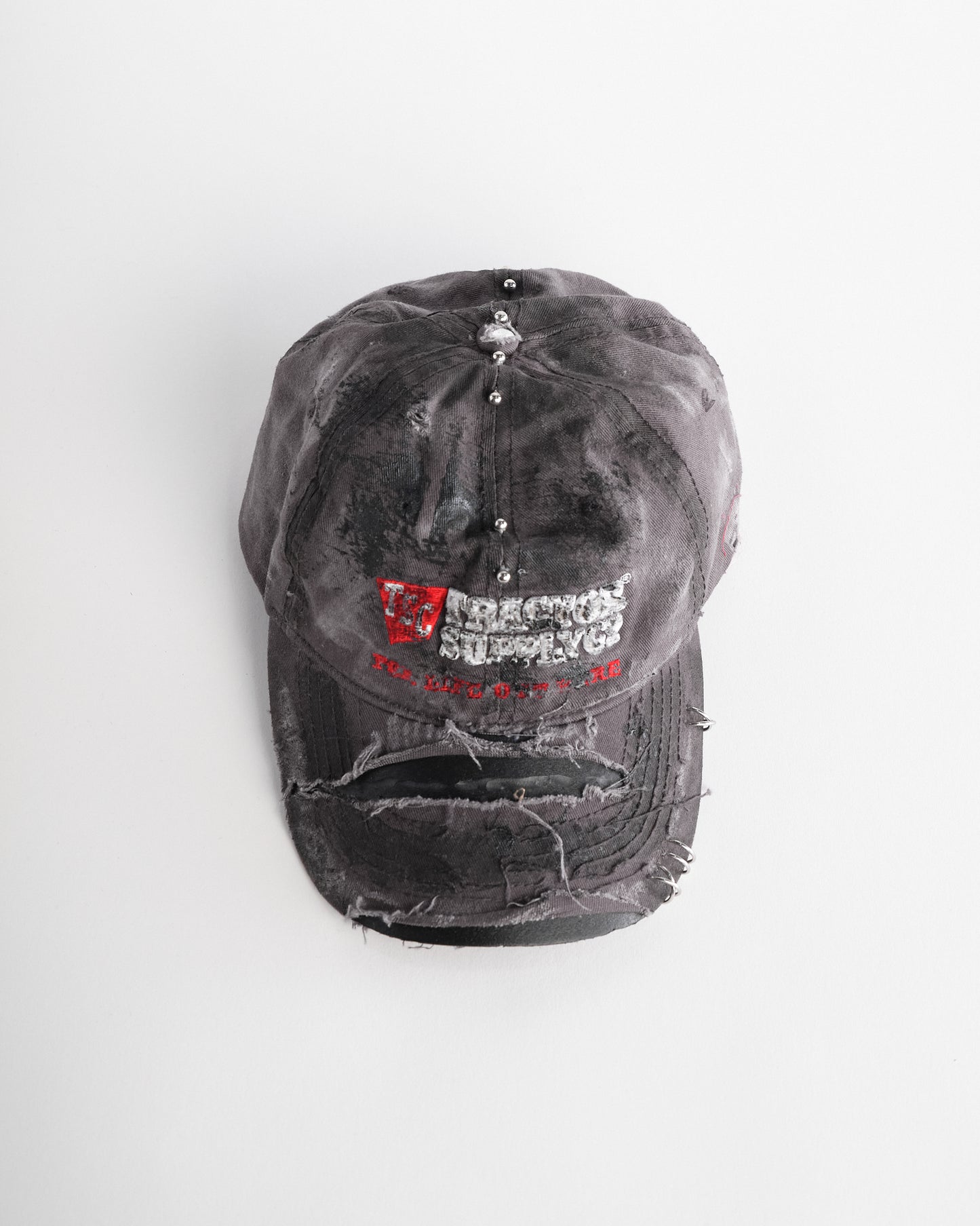 Overview of ASTROBOI* Tractor Supply grey hat with black paint distressing, stainless steel piercings, adjustable strap, handmade in NYC.