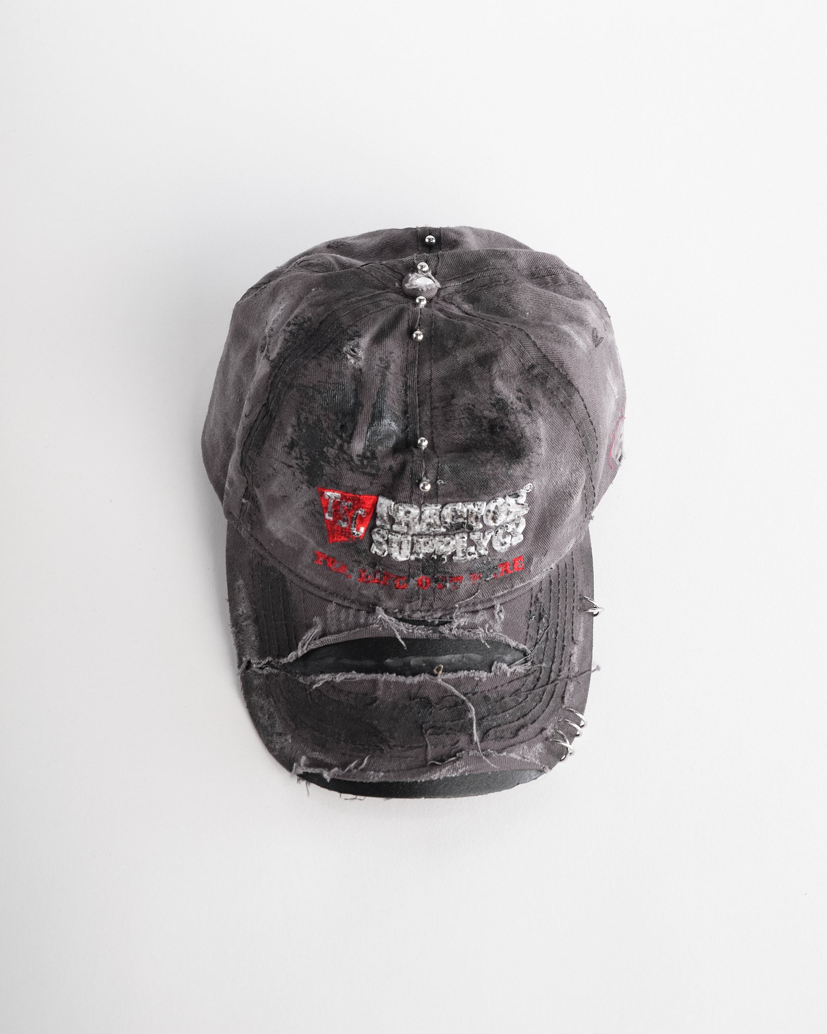Overview of ASTROBOI* Tractor Supply grey hat with black paint distressing, stainless steel piercings, adjustable strap, handmade in NYC.