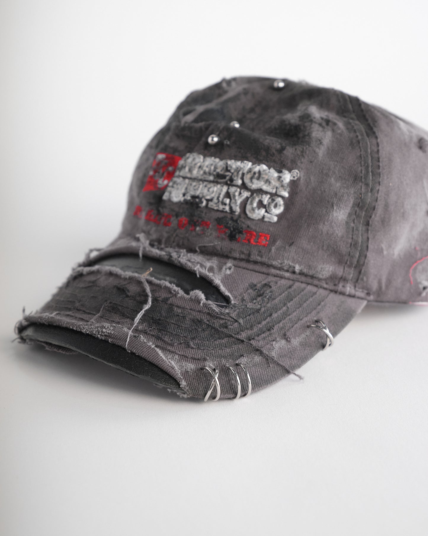 Left of ASTROBOI* Tractor Supply grey hat with black paint distressing, stainless steel piercings, adjustable strap, handmade in NYC.