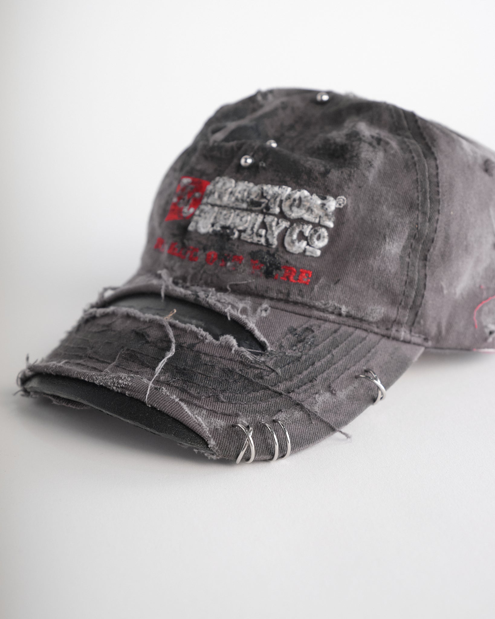 Left of ASTROBOI* Tractor Supply grey hat with black paint distressing, stainless steel piercings, adjustable strap, handmade in NYC.