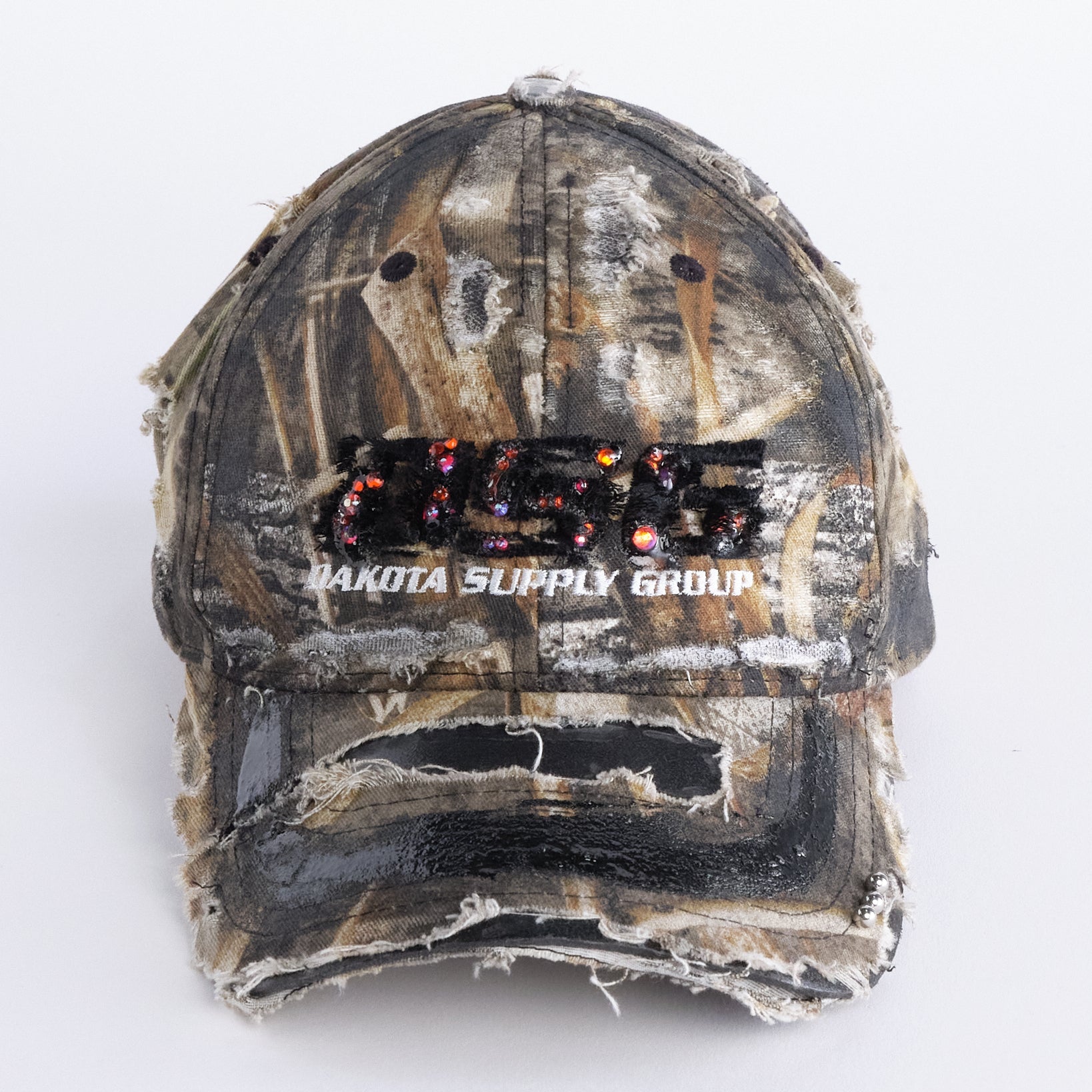 Front of ASTROBOI* DSG brown camouflage hat with rhinestone logo, black paint, clear resin accents, and stainless steel piercings, adjustable fit, handmade in NYC.