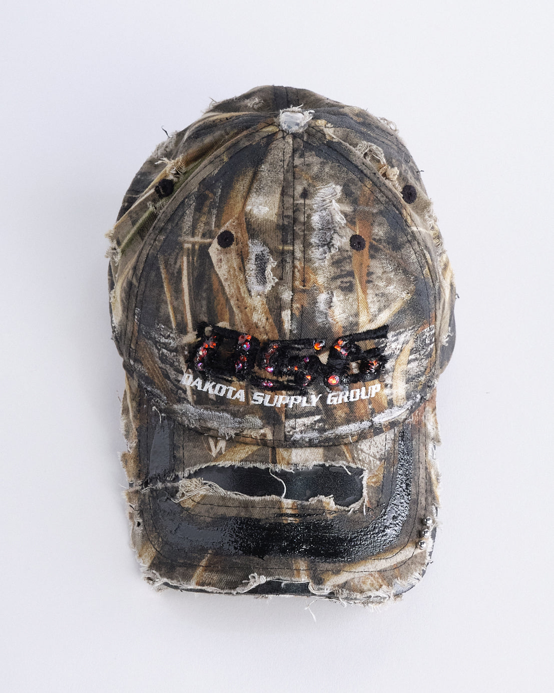 Front overview of ASTROBOI* DSG brown camouflage hat with rhinestone logo, black paint, clear resin accents, and stainless steel piercings, adjustable fit, handmade in NYC.