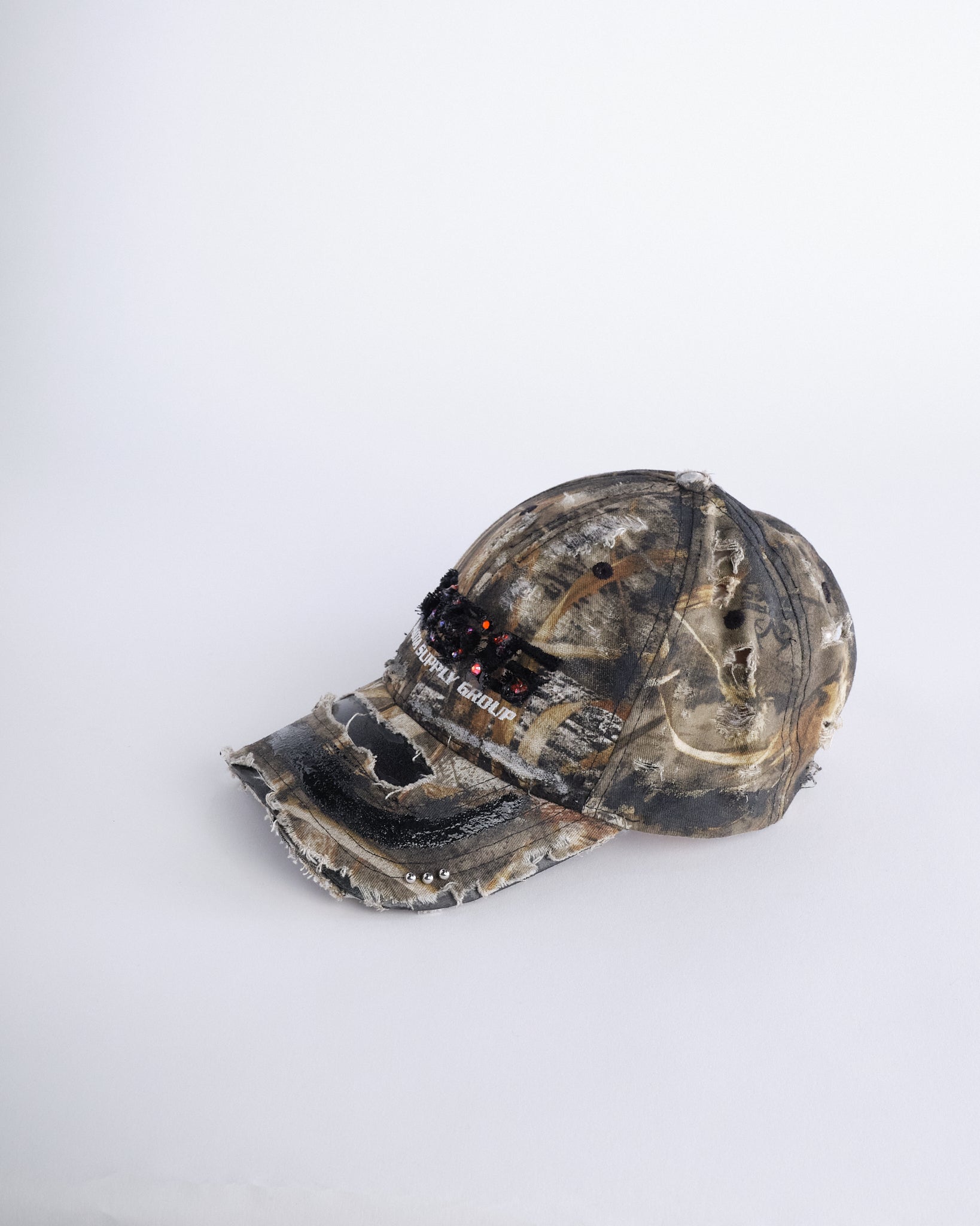 Left side of ASTROBOI* DSG brown camouflage hat with rhinestone logo, black paint, clear resin accents, and stainless steel piercings, adjustable fit, handmade in NYC.